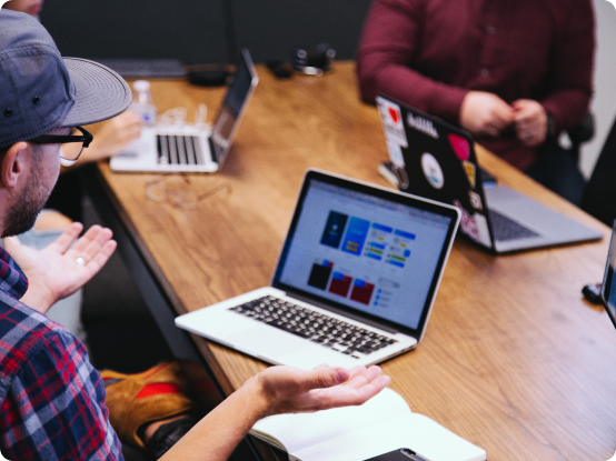A man sits behind his laptop, holding his hands up in despair